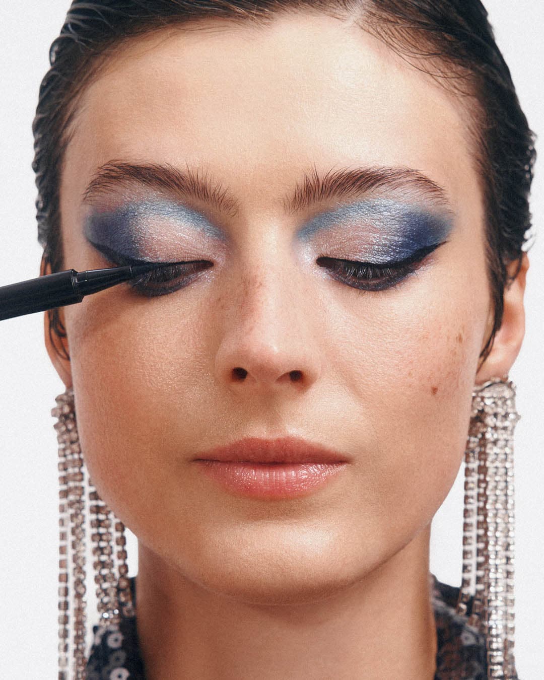 Moters veidas su užmerktomis akimis, ant vokų mėlyni šešėliai, juodas akių kontūro pieštukas paryškina viršutinę blakstienų liniją, o ausį puošia ilgas, blizgantis auskaras.