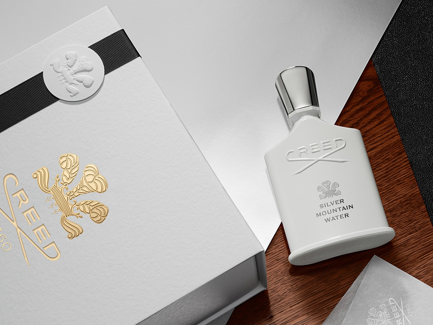 Das Creed Silver Mountain Water Eau de Parfum präsentiert sich in einem eleganten, weißen Flakon mit silbernem Verschluss und einer passenden Geschenkbox, die mit einem schwarzen Band verziert ist.