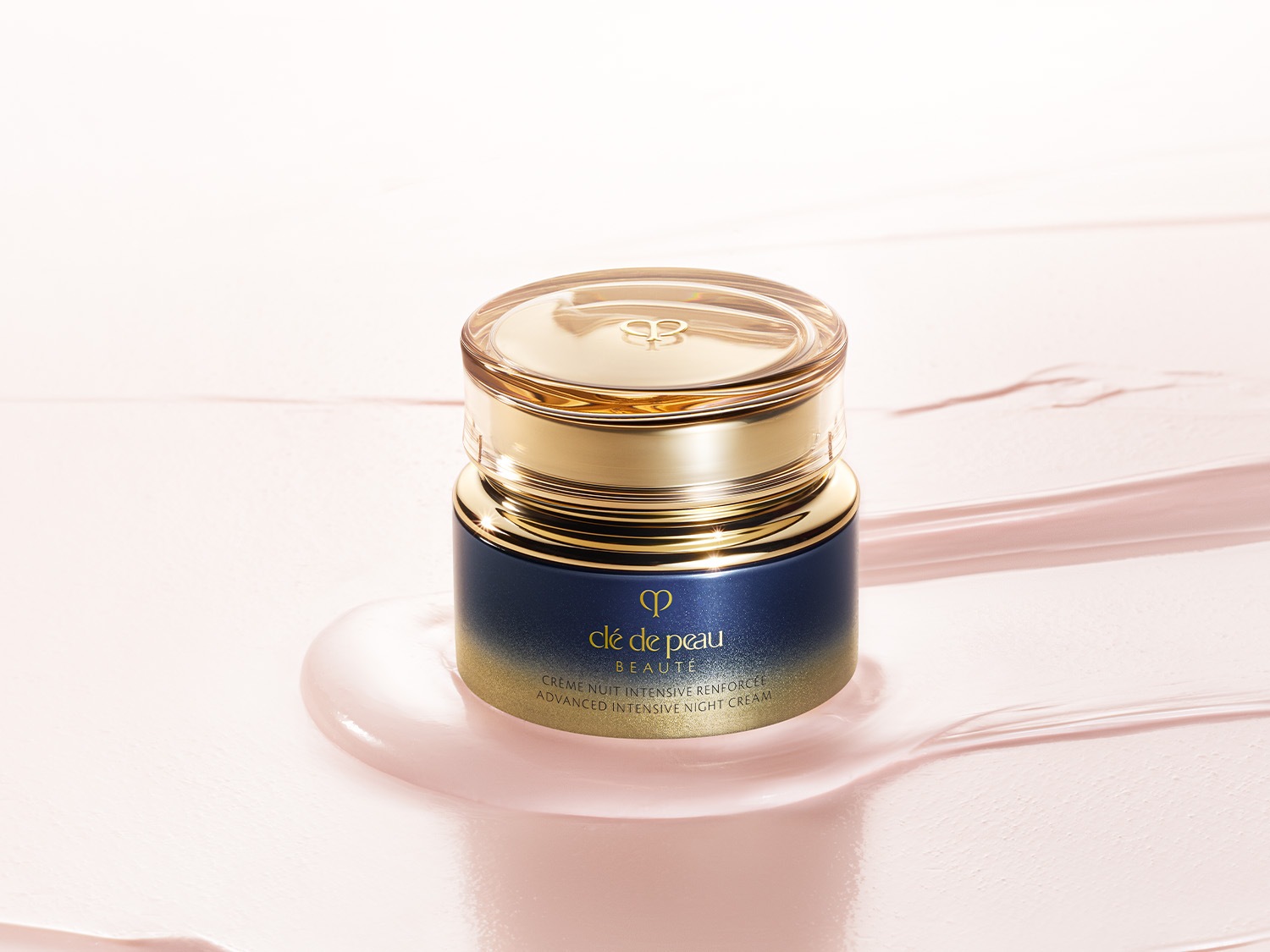Nahaufnahme eines Tiegel von Clé de Peau Beauté Crème Nuit Intensive Renforcée, dessen Verpackung von Marineblau zu Gold übergeht, auf einem rosa Untergrund.