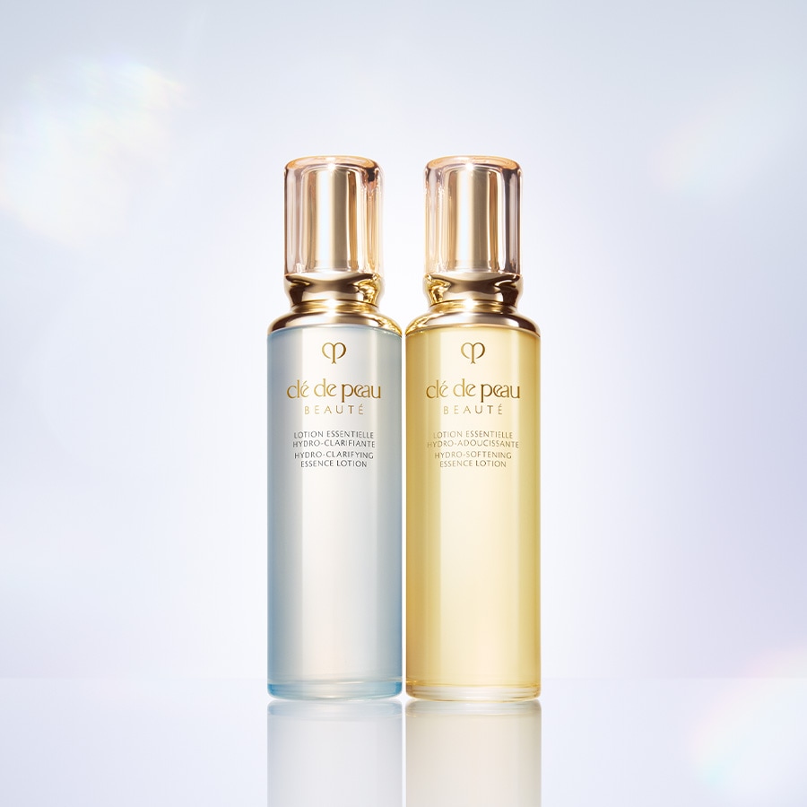 Zwei Flaschen Clé de Peau Beauté Essence Lotion, eine in einem hellblauen Farbton für die Hydro-Klärung und die andere in einem goldenen Farbton für die Hydro-Weichmachung, beide mit goldenen Verschlüssen.