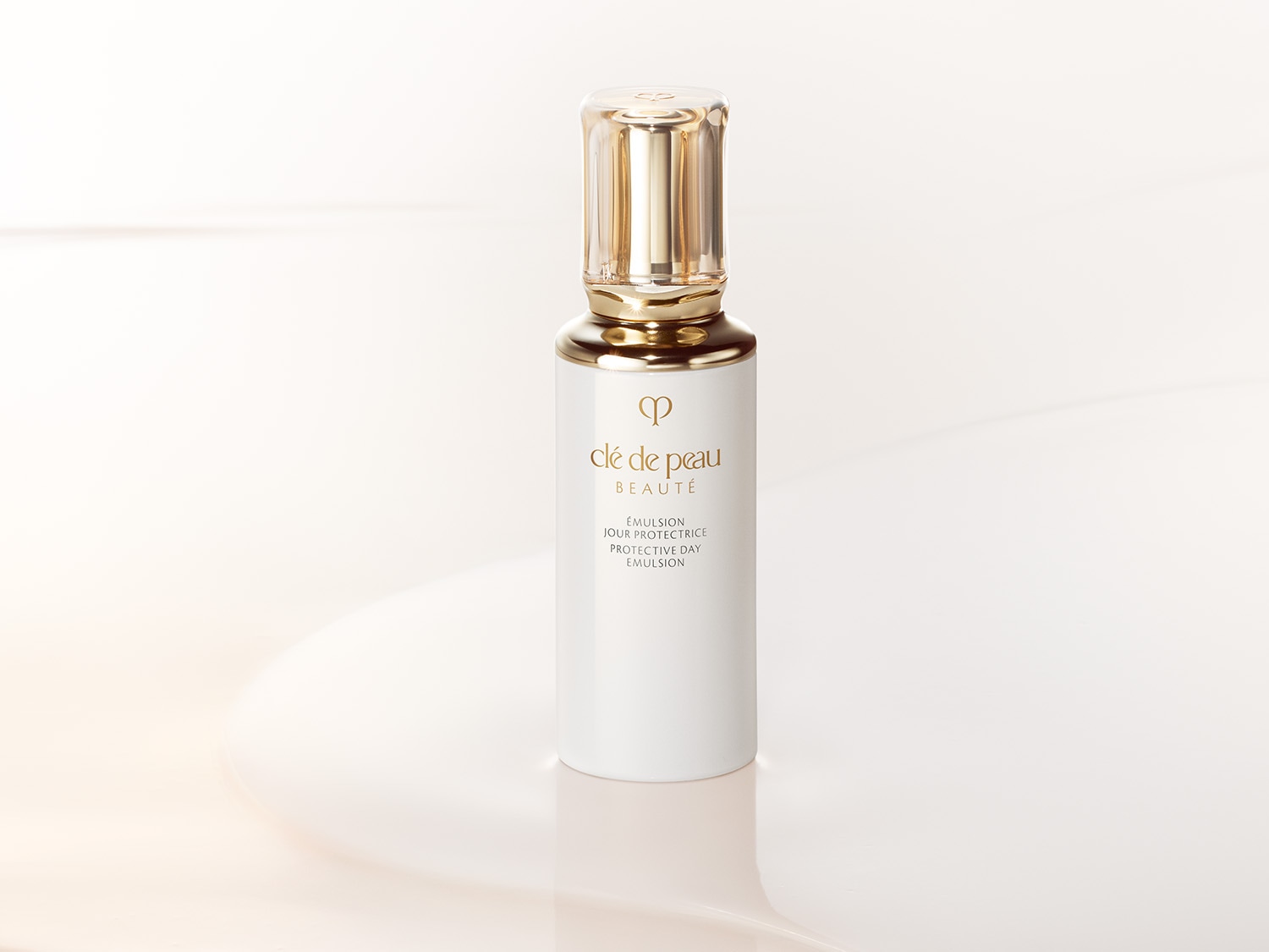 Weiße Flasche Clé de Peau Beauté Emulsion Jour Protectrice mit goldenem Verschluss, die Ihre Haut den ganzen Tag über mit Feuchtigkeit versorgt und schützt.