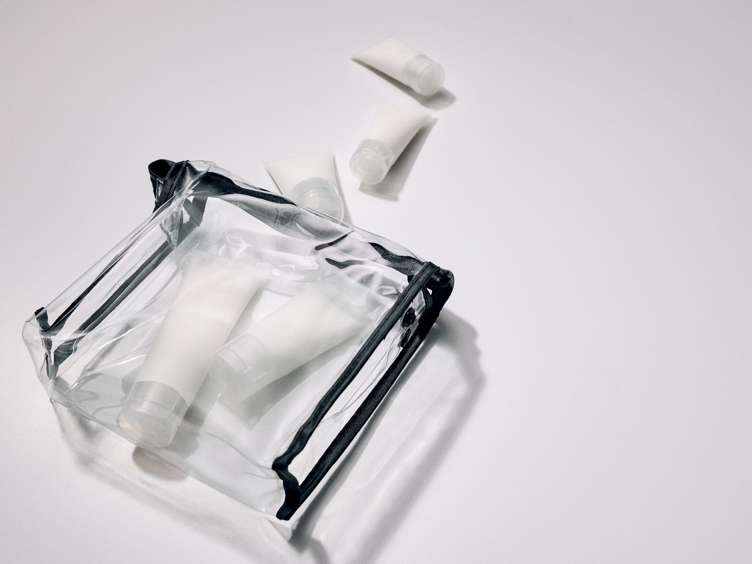 Transparante toilettas met zwarte ritssluiting, gevuld met witte tubes en losse tubes ernaast.