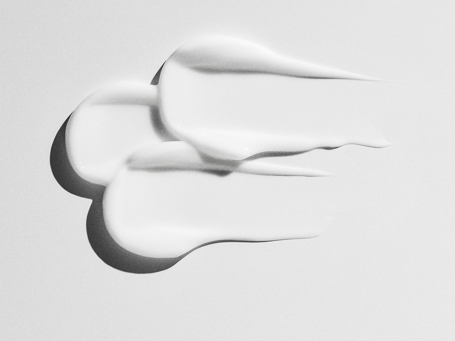 Drie streken witte, dikke crème liggen op een witte achtergrond en vormen een abstract patroon.