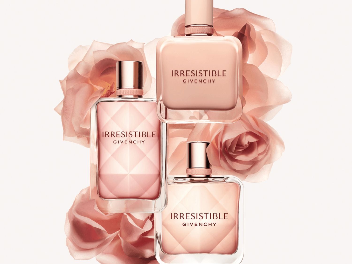 Három rózsaszín Givenchy Irresistible parfümös üveg látható rózsaszín rózsák előtt.