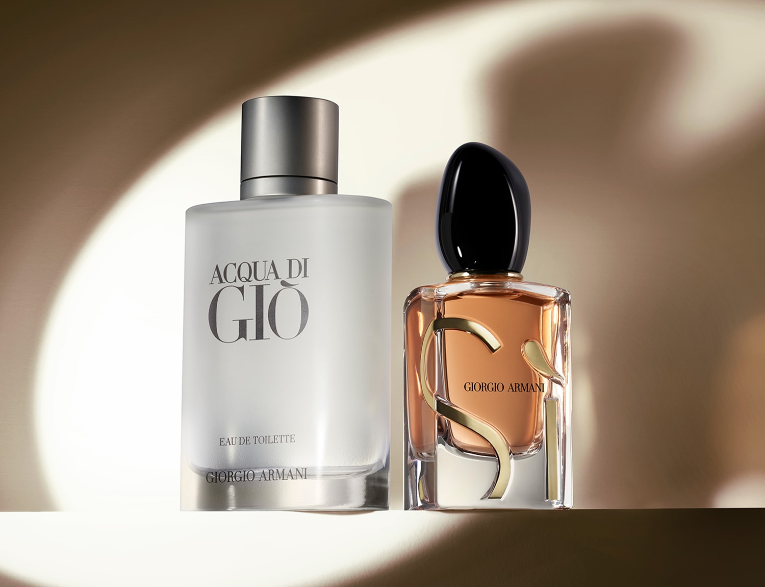 Dva flakony parfémů Giorgio Armani: Acqua di Giò s matným sklem a stříbrným uzávěrem a Sì s hnědou tekutinou a černým uzávěrem.