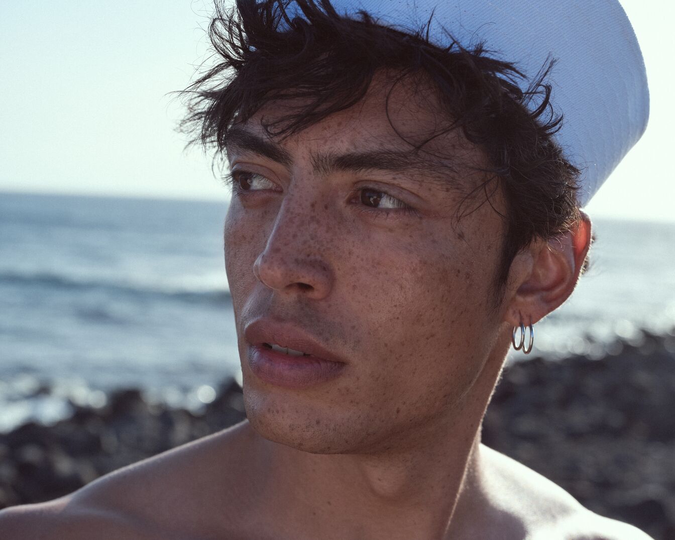 Portret van een man met sproeten en een witte matrozenpet, kijkend naar de horizon boven de zee.