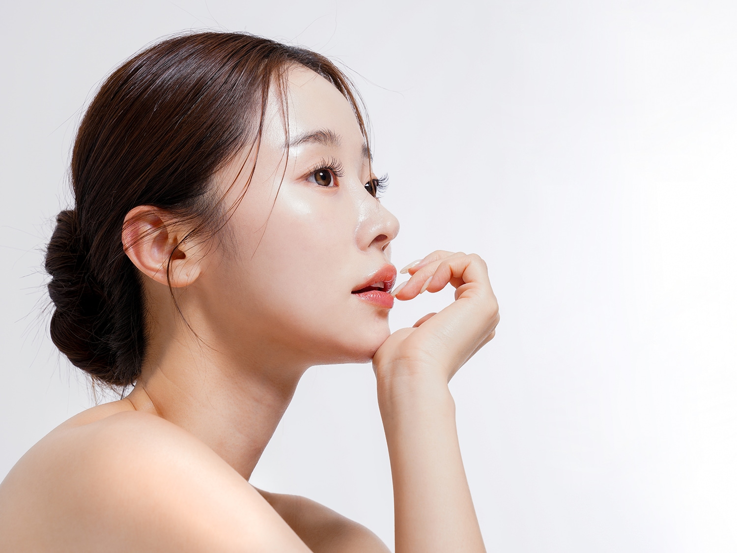 Profil einer Frau mit glänzender Haut, die ihr Kinn mit der Hand berührt und einen Dutt trägt.