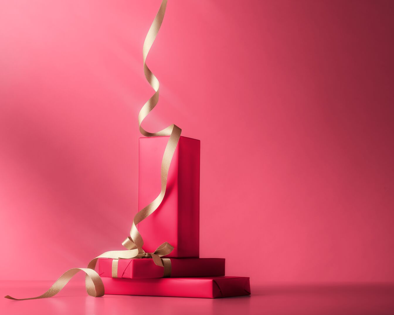 Trois cadeaux emballés dans du papier rose vif sont empilés les uns sur les autres et décorés d'un ruban doré.