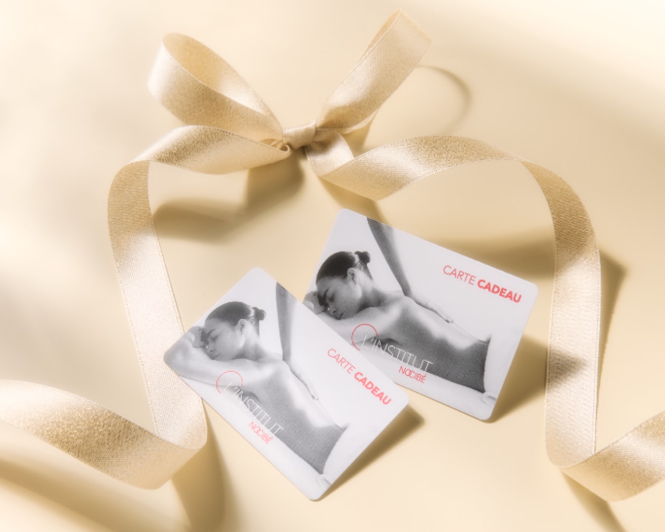 Deux cartes cadeaux L'INSTITUT NOCIBÉ sont décorées avec un ruban doré, offrant une expérience de détente et de bien-être.
