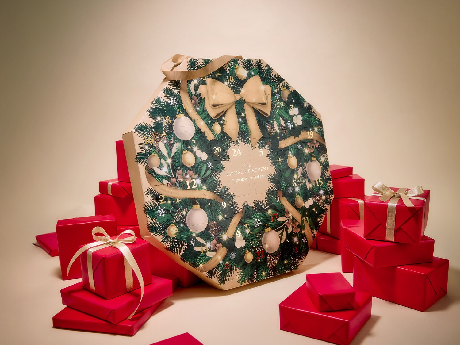 Découvrez le calendrier de l'Avent Rituals, orné d'une couronne festive et entouré de cadeaux rouges élégants, pour un compte à rebours magique jusqu'à Noël.