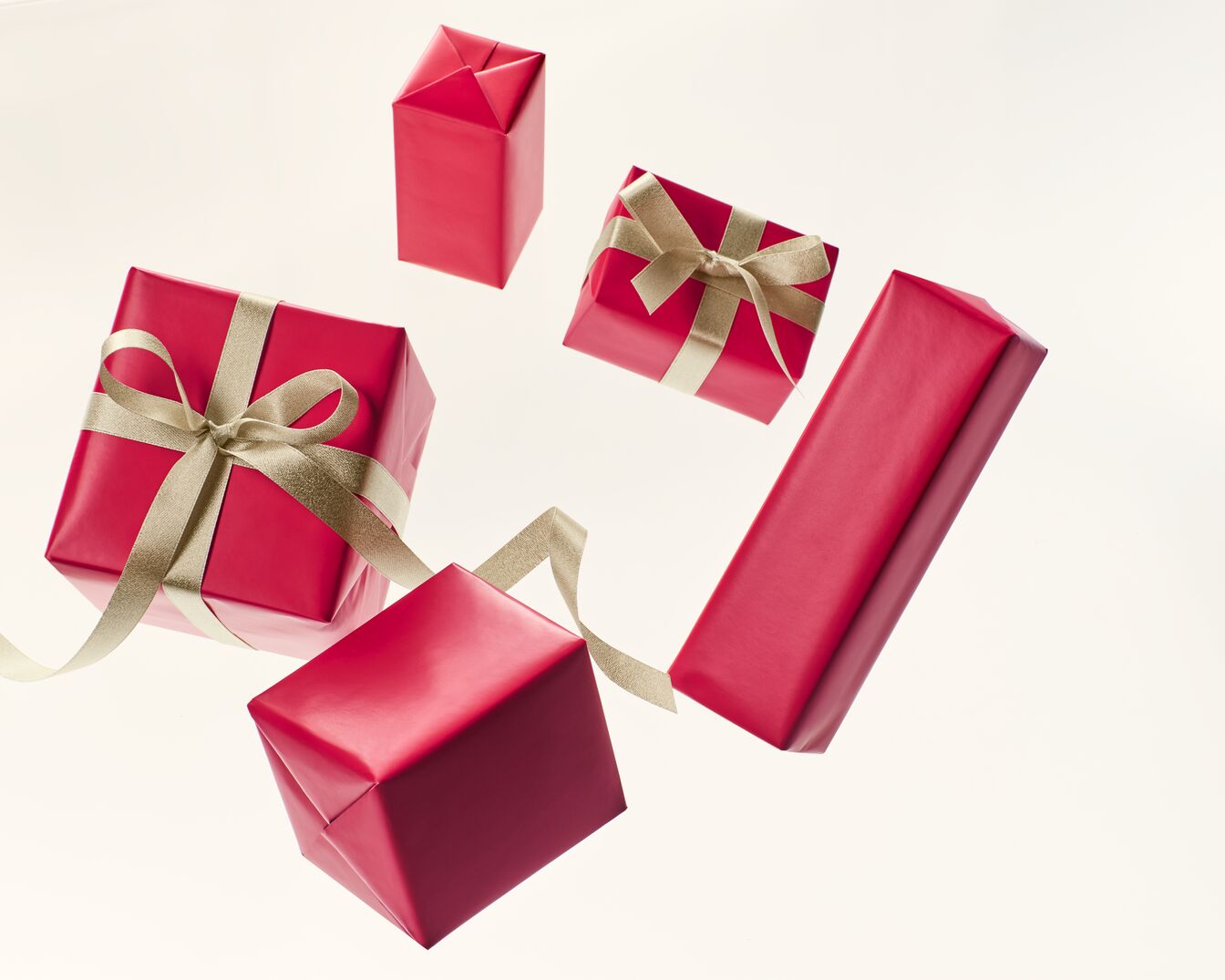 Une collection de cadeaux emballés dans du papier rouge vif et ornés d'élégants rubans dorés, flottant dans un arrangement festif.
