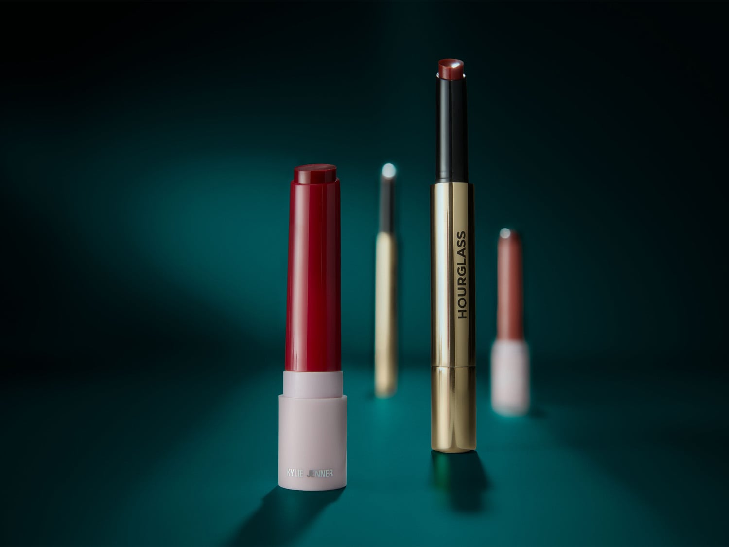 Szminki Kylie Jenner i Hourglass w odcieniach czerwieni i złota na ciemnym tle, idealne do podkreślenia ust.