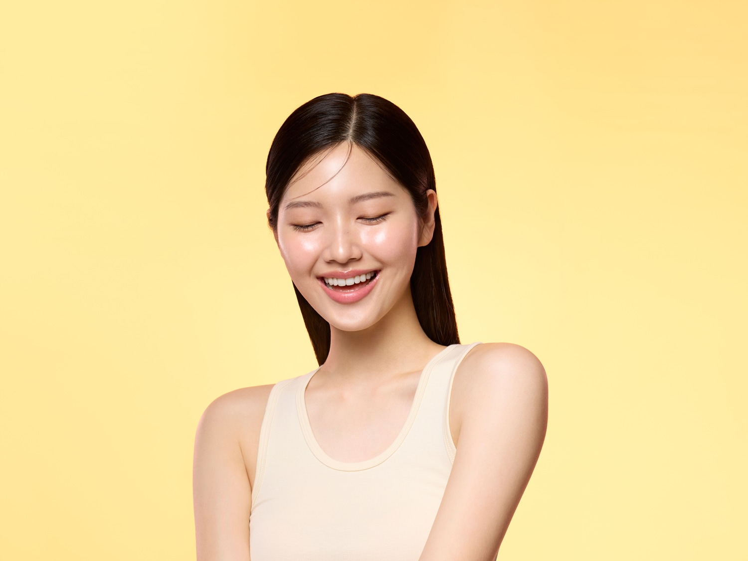 Een stralende jonge vrouw met een heldere huid en een brede glimlach tegen een gele achtergrond.