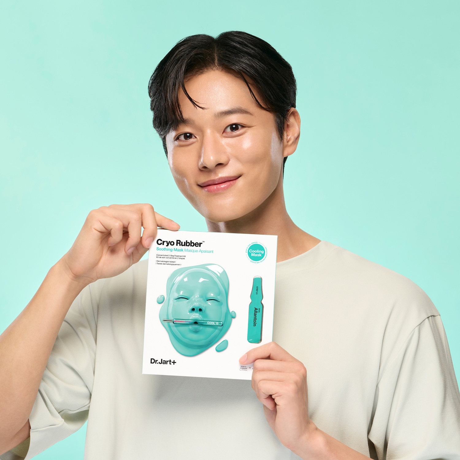 Een man houdt een Dr.Jart+ Cryo Rubber Soothing Mask vast, met een afbeelding van een blauw masker en een ampul met Allantoïne.