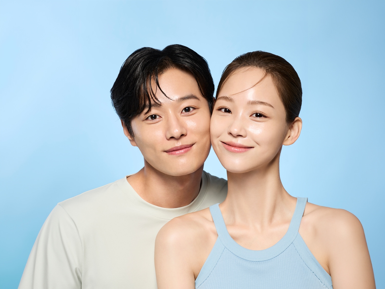 Een stralend koppel lacht, de man met een wit shirt en de vrouw met een blauwe top, tegen een zachtblauwe achtergrond.
