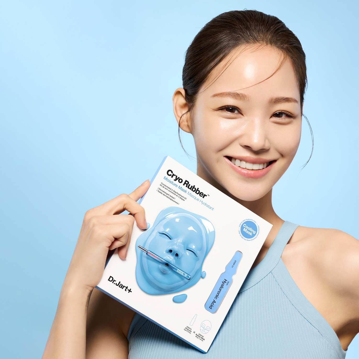 Een stralende vrouw toont de Dr. Jart+ Cryo Rubber Moisture Mask, een hydraterend masker met hyaluronzuur voor een verkoelende en verzorgende gezichtsbehandeling.