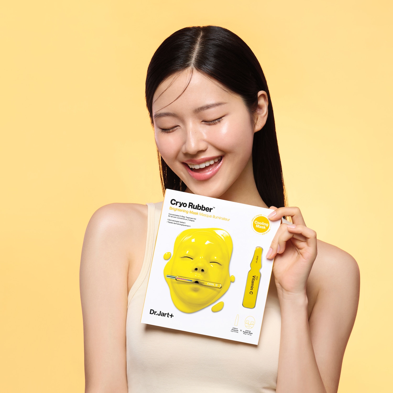 Een stralende vrouw houdt Dr.Jart+ Cryo Rubber Brightening Mask vast, een geconcentreerde 2-staps behandeling met vitamine C voor een verhelderende en verkoelende maskerervaring.