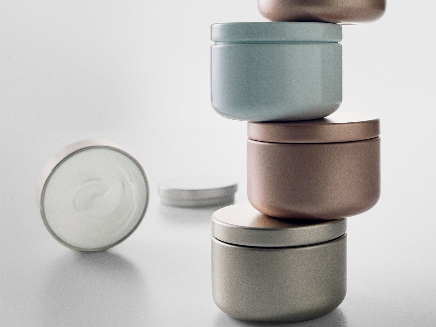 Gestapelte Döschen in Pastellfarben und Metallic-Tönen, daneben eine offene Dose mit weißer Creme.