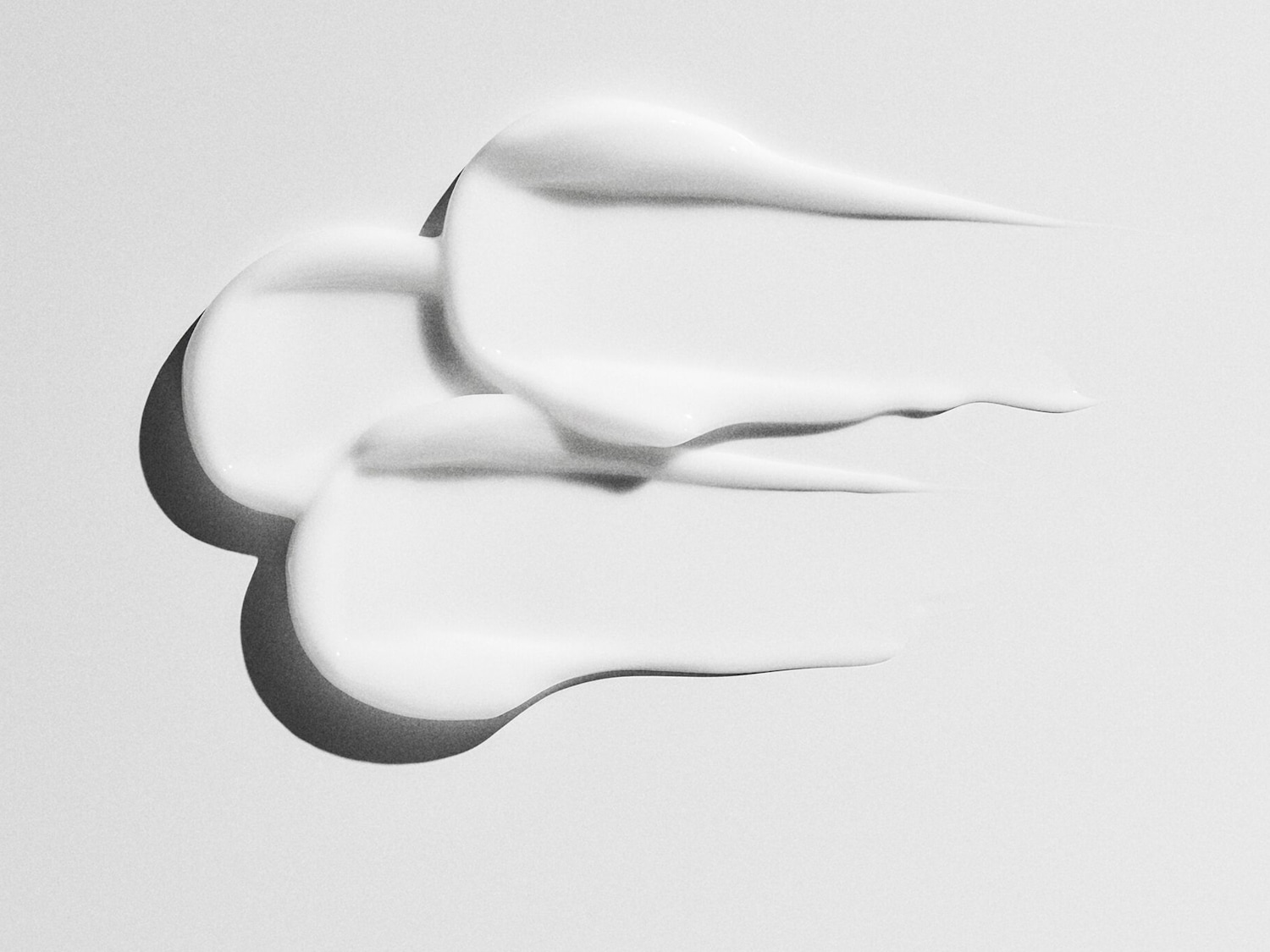 Drie streken witte, dikke crème liggen op een witte achtergrond en vormen een abstract patroon.