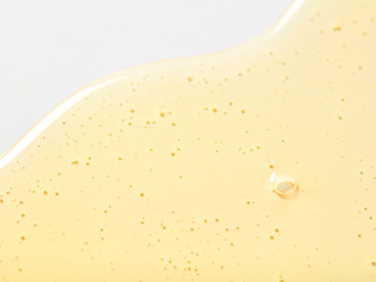 Gouden serumtextuur met kleine luchtbelletjes, ideaal voor het hydrateren en voeden van de huid.