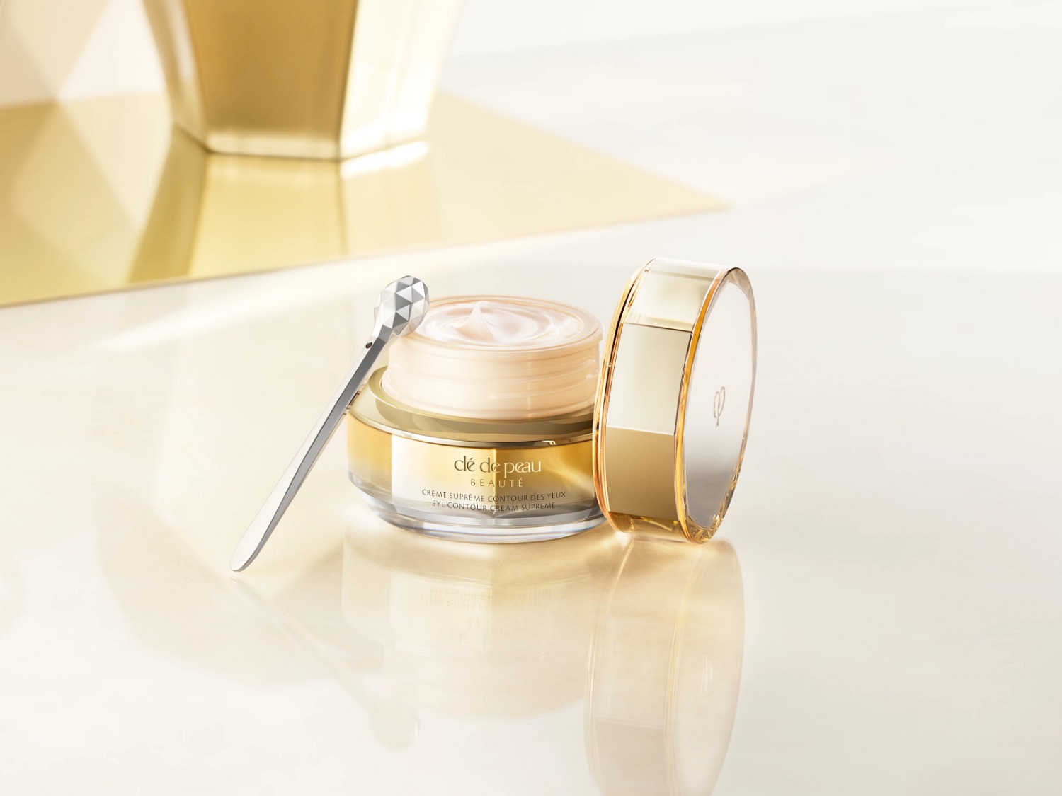 Découvrez la Crème Suprême Contour des Yeux Clé de Peau Beauté, présentée dans un élégant pot doré avec un applicateur argenté, promesse d'un soin luxueux pour un regard éclatant.