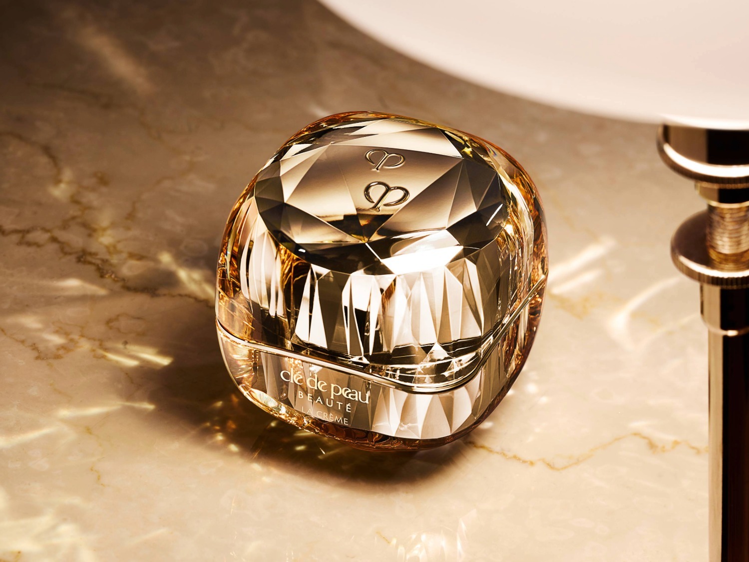 Découvrez le luxe avec le pot de crème Cle de Peau Beauté, un écrin doré taillé comme un diamant, promesse d'une peau éclatante.