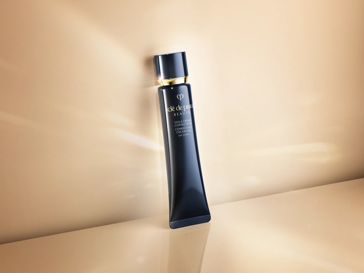 Voici un tube bleu marine de Clé de Peau Beauté Voile Crème Correcteur avec un bouchon noir et des détails dorés, conçu pour unifier et protéger la peau.