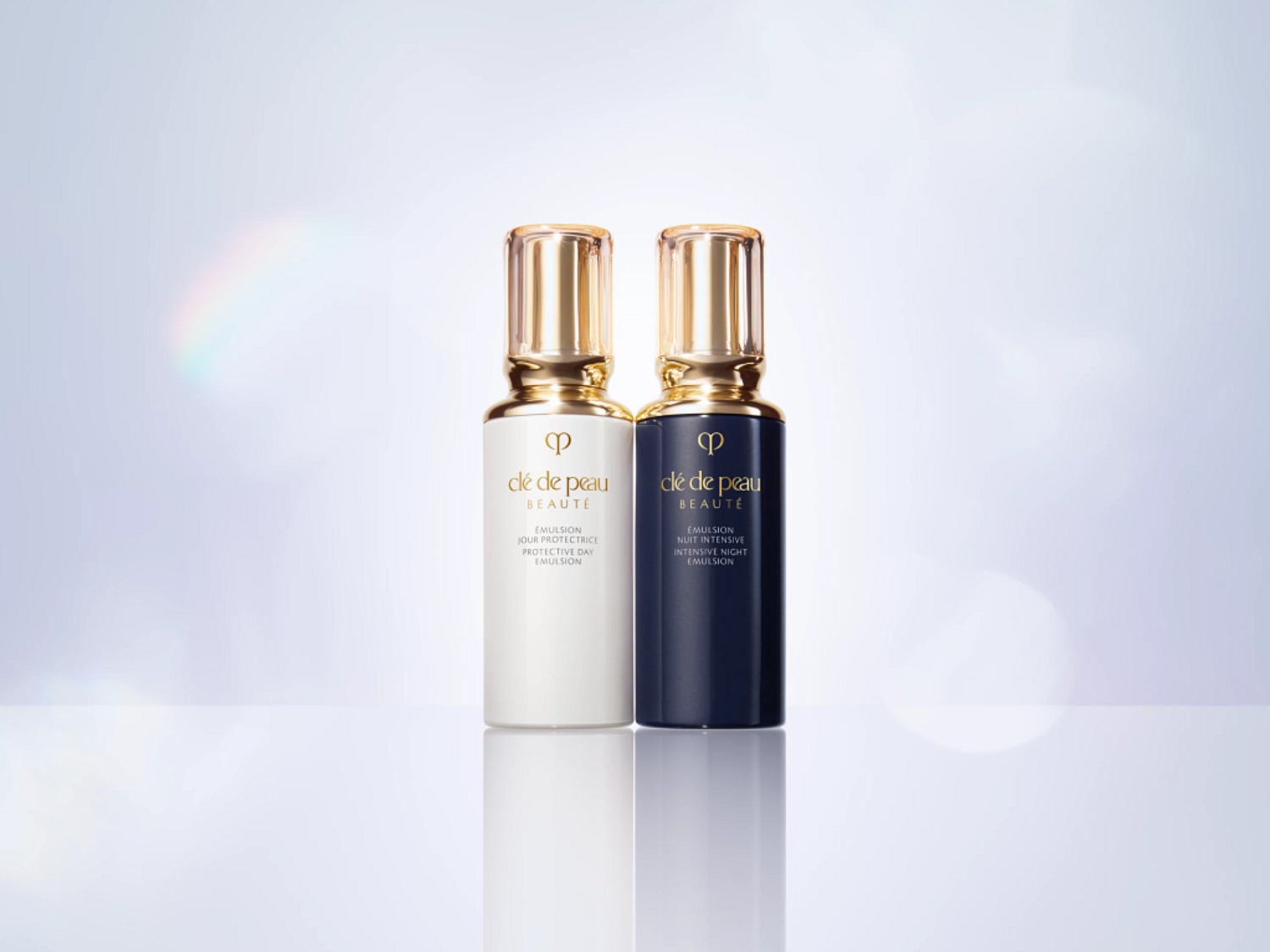 Voici l'émulsion de jour protectrice et l'émulsion de nuit intensive Clé de Peau Beauté, présentées dans des flacons élégants avec des bouchons dorés.