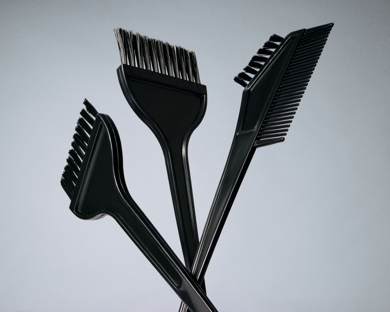 Nahaufnahme von drei schwarzen Färbepinseln und einem Kamm, die zum Auftragen von Farbe auf das Haar verwendet werden.