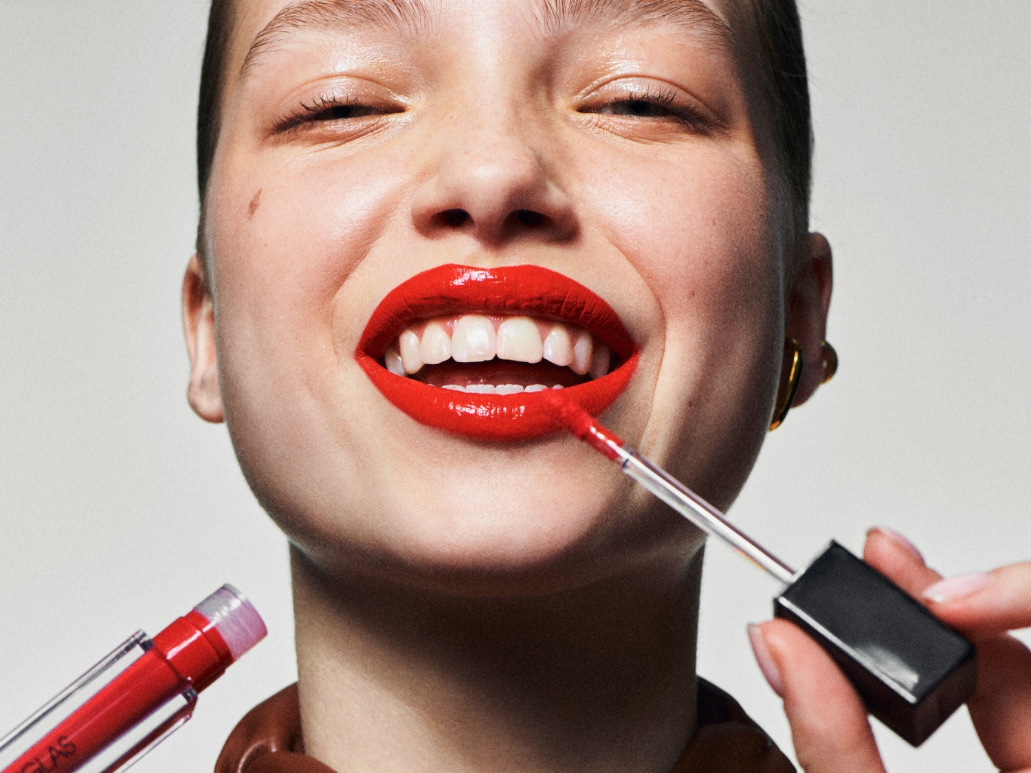 Een stralende vrouw lacht terwijl ze een helderrode lipgloss aanbrengt, de glanzende textuur accentueert haar lippen.