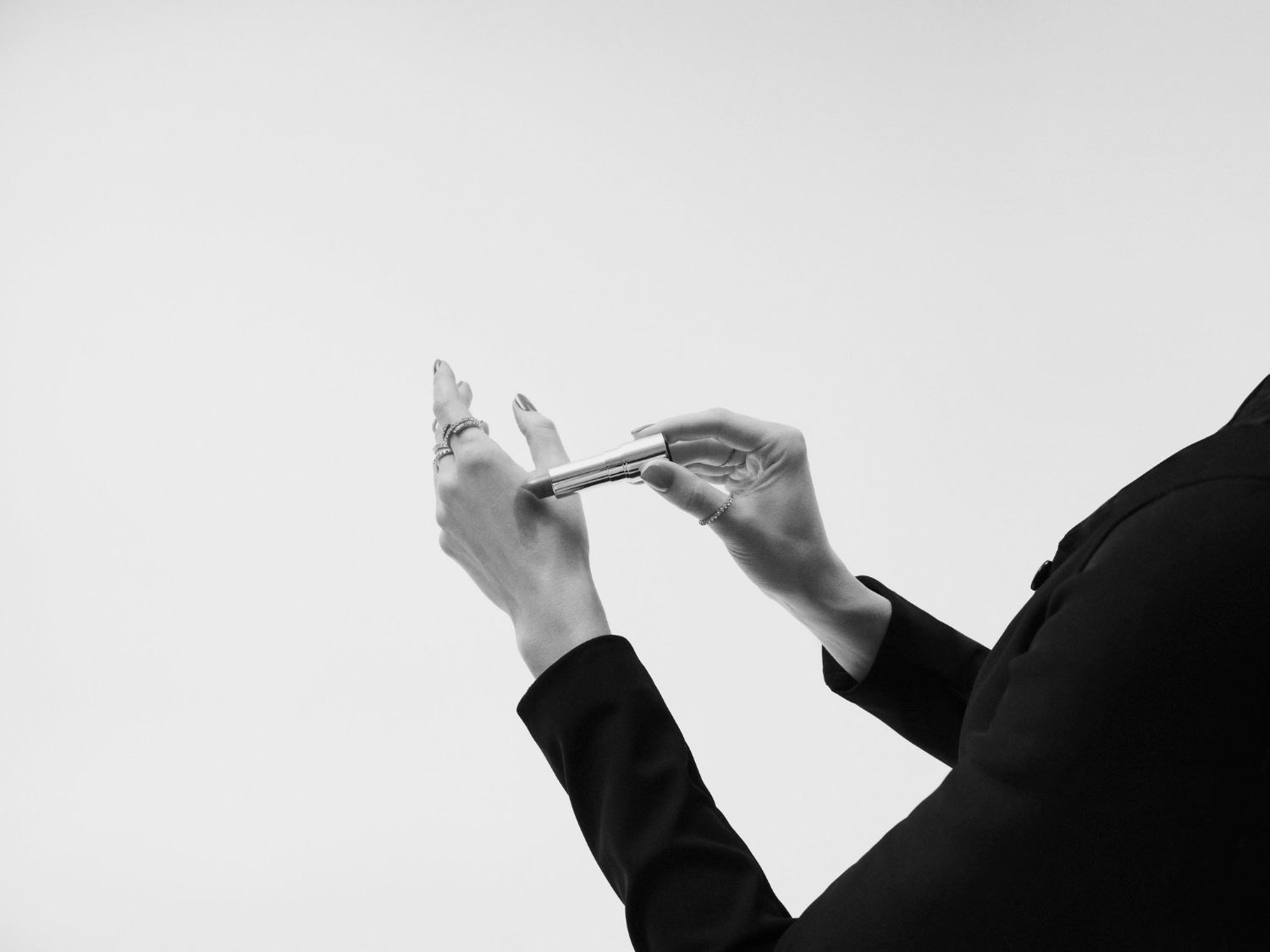 Een vrouw in een zwart jasje houdt een zilveren lippenstift vast, klaar om haar lippen te accentueren met een vleugje kleur.