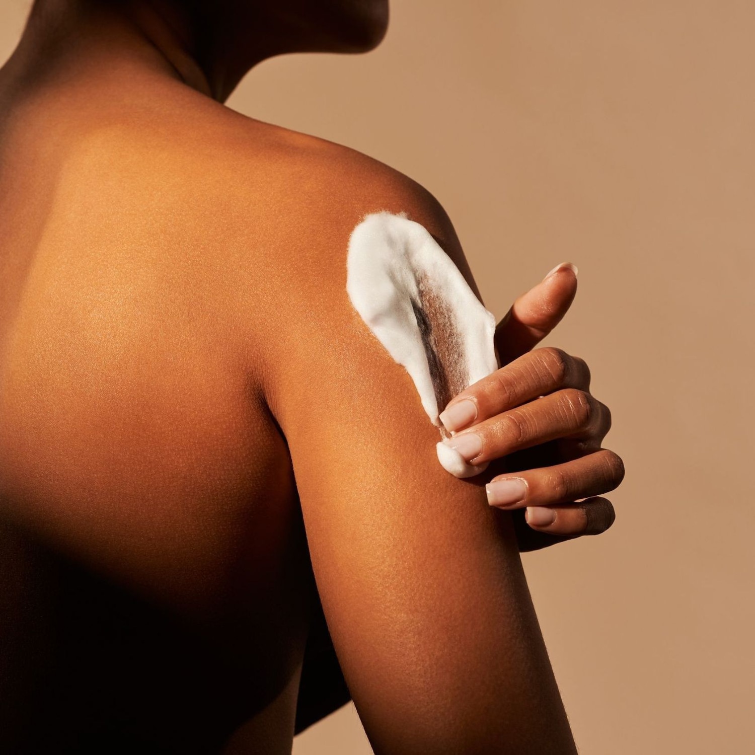 Een vrouw smeert een witte crème op haar schouder, waarbij de zachte textuur en hydraterende werking van het product worden benadrukt.