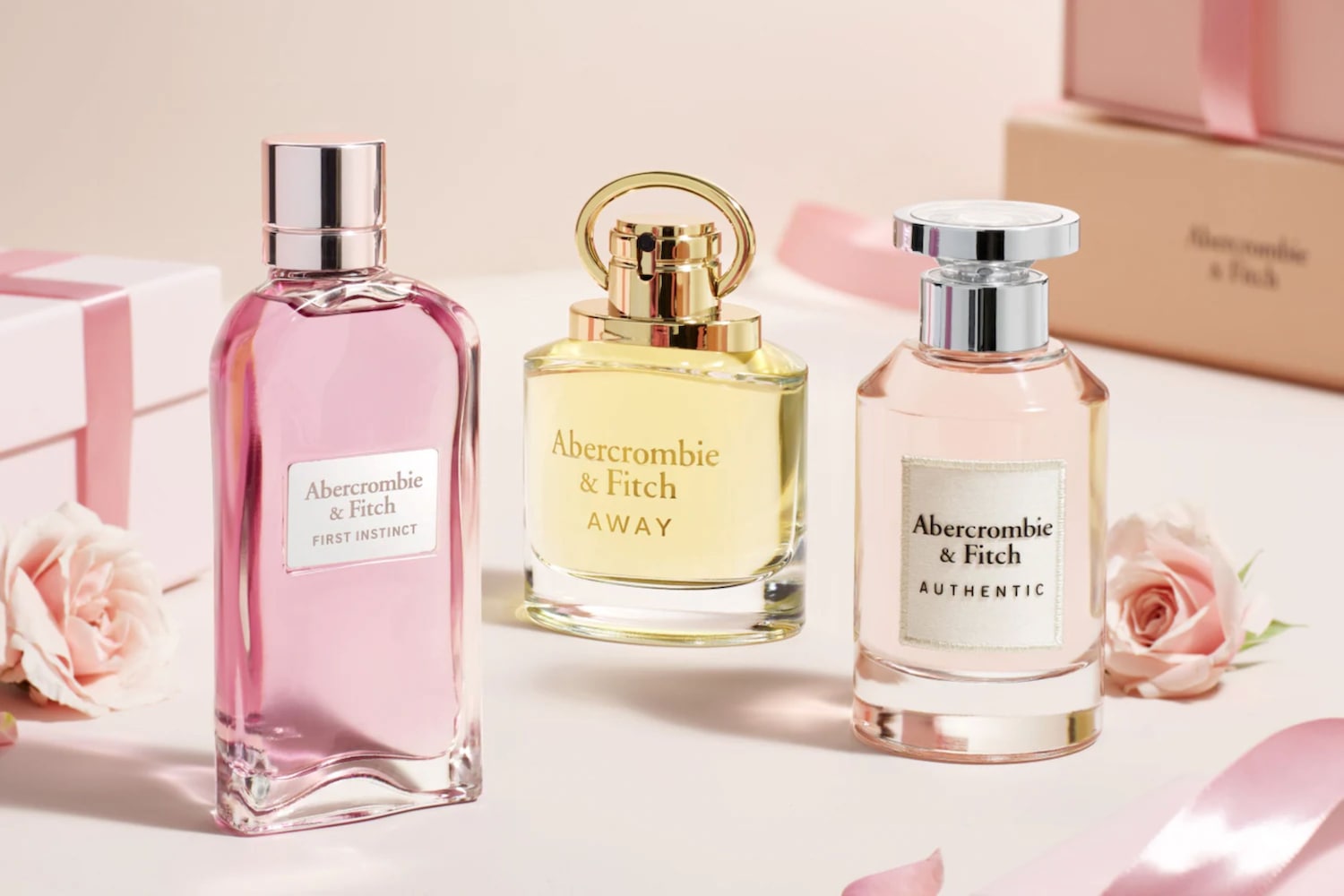 Drei Flakons Abercrombie & Fitch Parfüm stehen auf einem Tisch, von links nach rechts: First Instinct mit rosa Flüssigkeit, Away mit gelber Flüssigkeit und Authentic mit hellrosa Flüssigkeit.