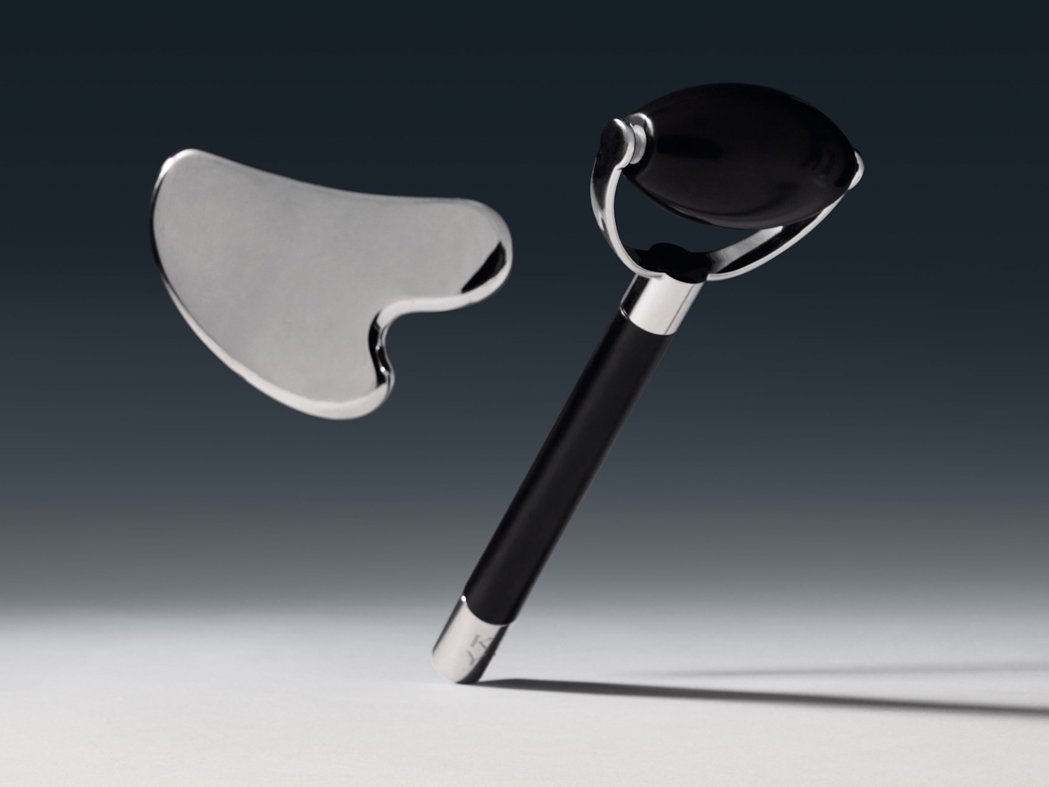 Gezichtsverzorgingsset met een zilverkleurige gua sha steen en een zwarte gezichtsroller met een zilverkleurig handvat, voor een ontspannende gezichtsmassage.