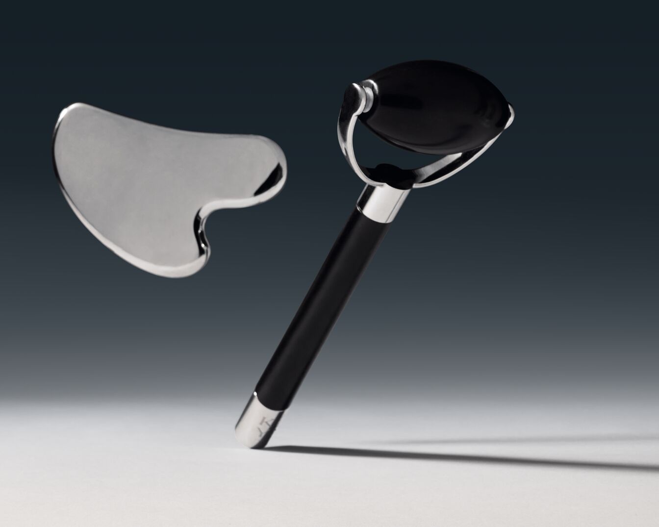 Zwarte gezichtsroller met zilveren details en een zilveren gua sha-steen voor een ontspannende gezichtsmassage.