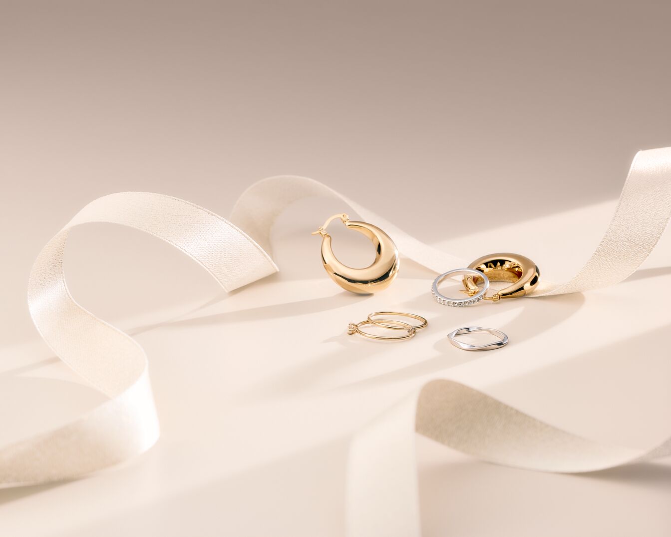 Nahaufnahme von goldenen Creolen und Ringen, die elegant auf einem cremefarbenen Band drapiert sind und einen Hauch von Luxus und Stil ausstrahlen.