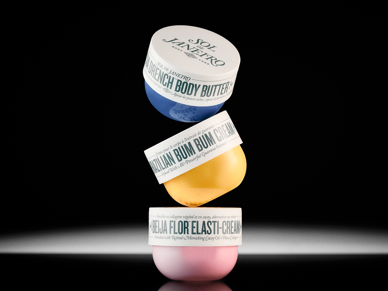 Stapel von Sol de Janeiro Körperpflegeprodukten: Drench Body Butter in Blau, Brazilian Bum Bum Cream in Gelb und Beija Flor Elasti-Cream in Rosa.