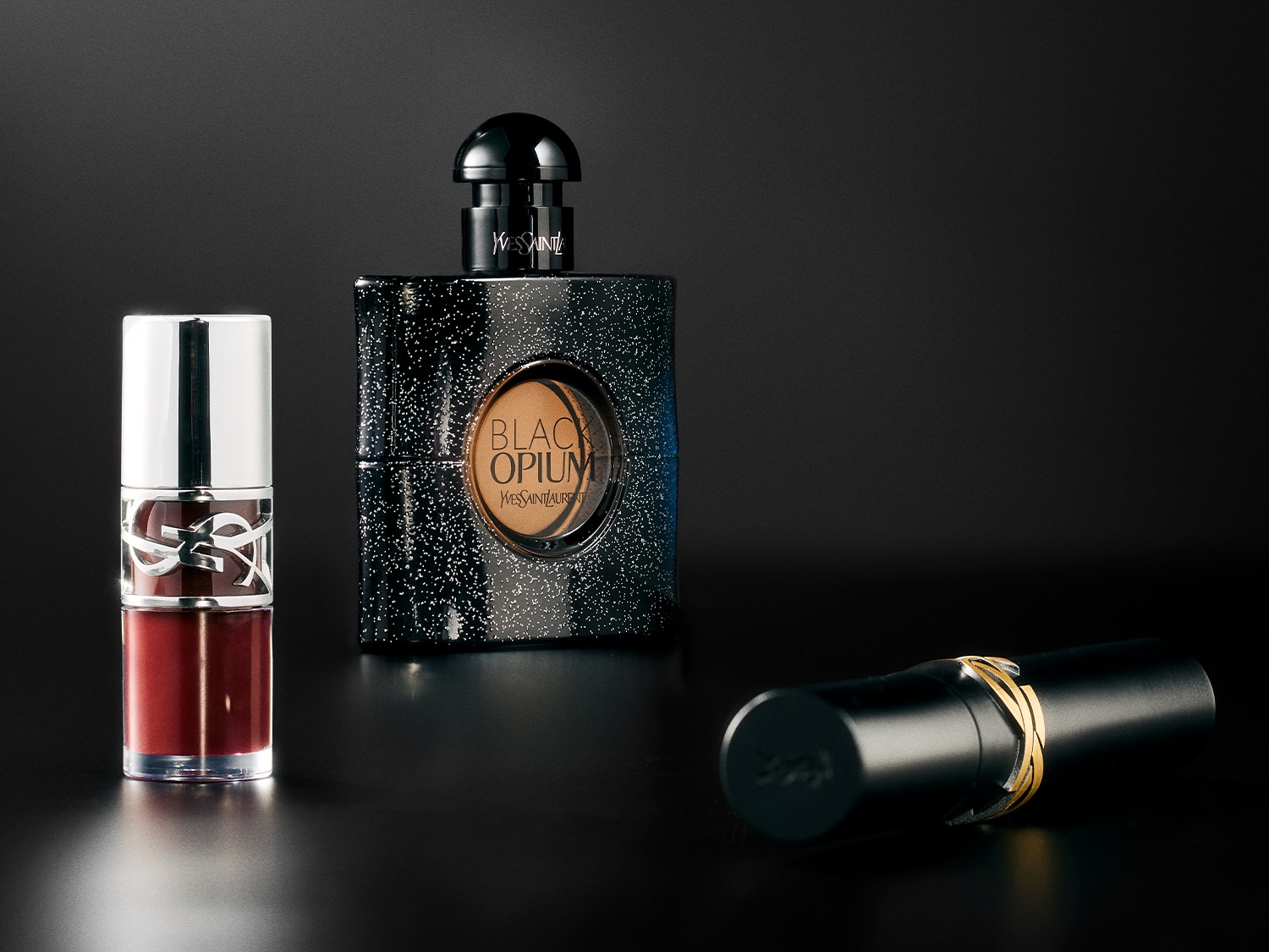 Entdecke das Yves Saint Laurent Black Opium Eau de Parfum, einen Lipgloss mit dunkler Tönung und einen schwarzen Lippenstift mit goldenem Ring.