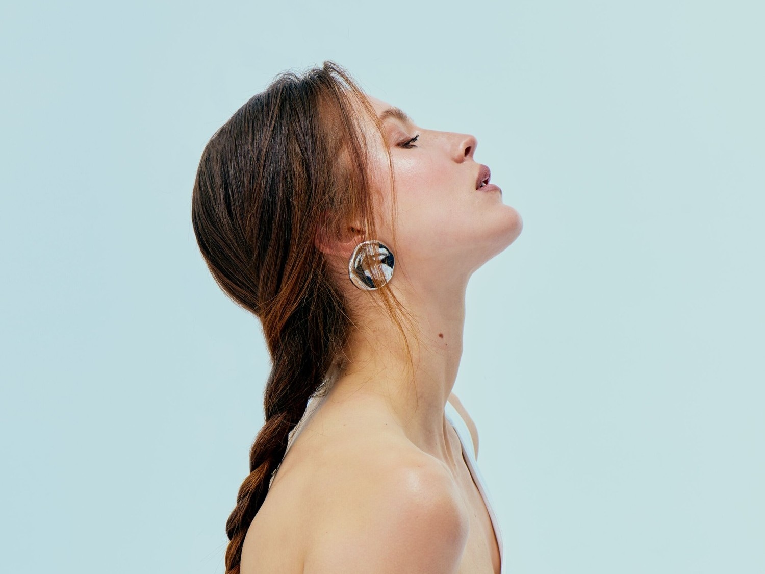 Eine Frau mit braunem Zopf und silbernen Ohrringen blickt mit geschlossenen Augen und leicht geöffnetem Mund nach oben.