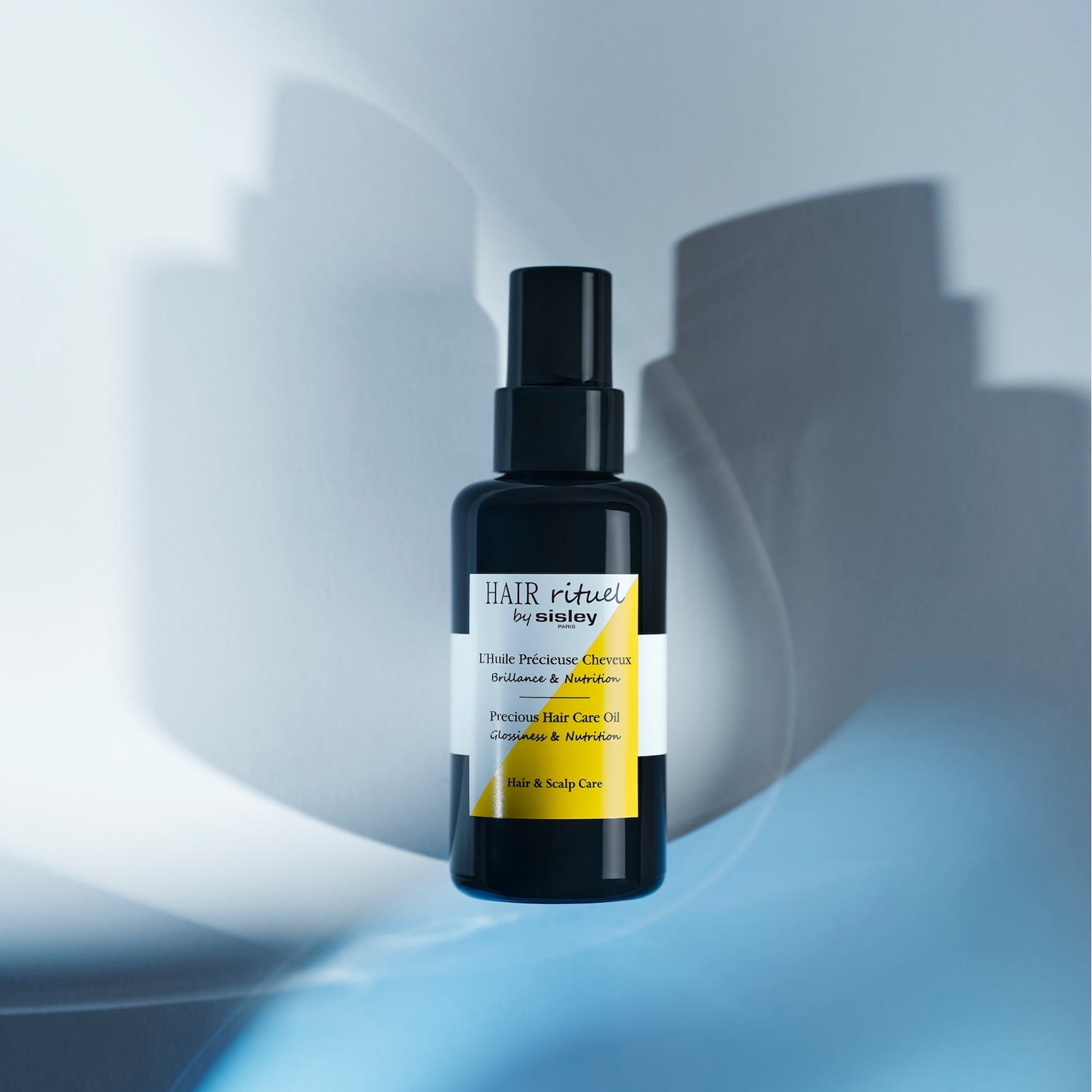 Czarna butelka Hair Rituel by Sisley Paris, cenny olejek do włosów zapewniający blask i odżywienie, przeznaczony do pielęgnacji włosów i skóry głowy.