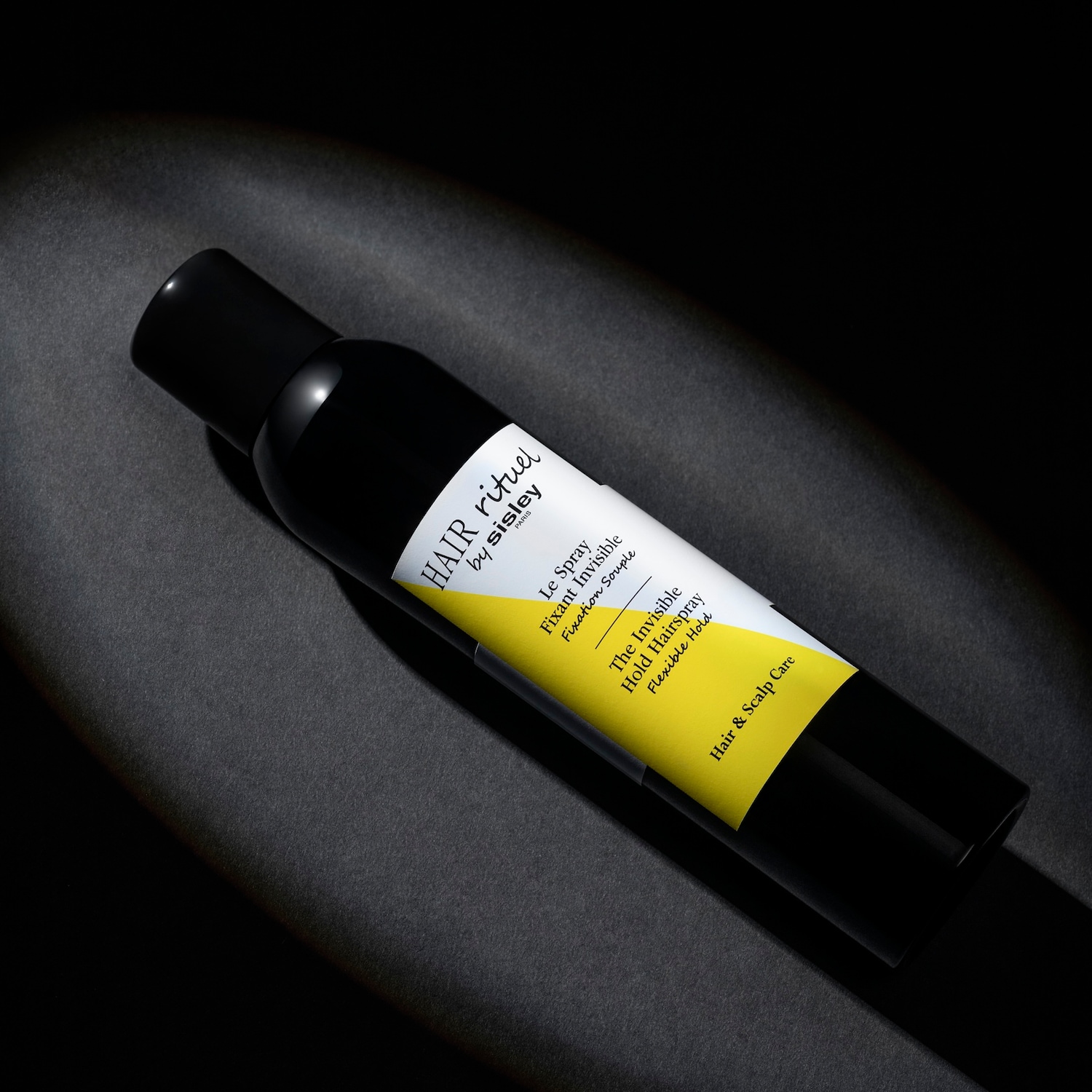 Czarna butelka lakieru do włosów Hair Rituel by Sisley z żółtą etykietą, na której widnieje napis: „The Invisible Hold Hairspray Flexible Hold”.