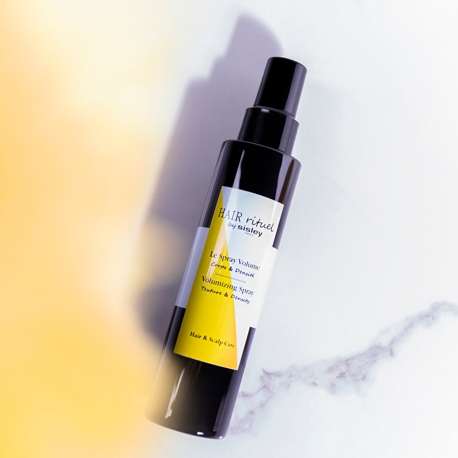 Czarna butelka Hair Rituel by Sisley Le Spray Volume, który dodaje włosom tekstury i gęstości, zapewniając pielęgnację włosów i skóry głowy.