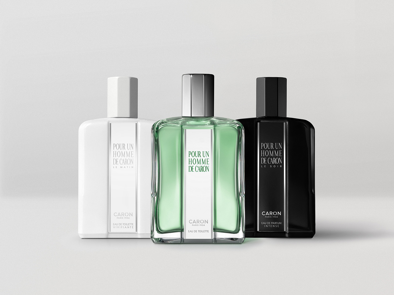 Trzy flakony perfum Caron Pour Un Homme: biały "Le Matin", zielony i czarny "Le Soir", każdy z srebrnym napisem.