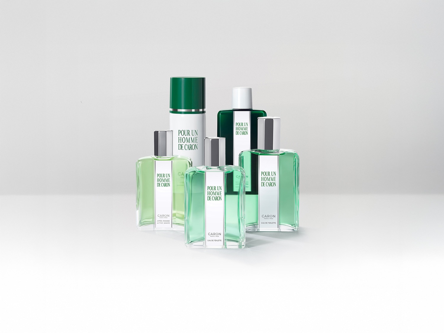 Zdjęcie przedstawia grupę produktów Caron Pour Un Homme, w tym wody toaletowe i balsamy po goleniu, wszystkie w odcieniach zieleni i srebra, tworzące elegancką kompozycję.