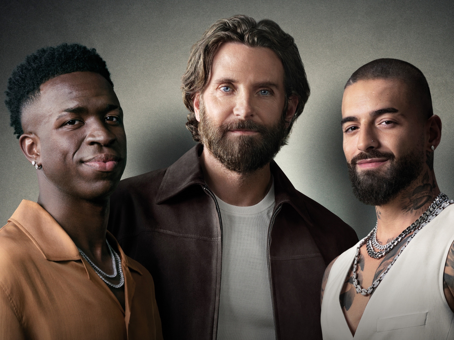 Na portrecie trzech mężczyzn o różnym pochodzeniu etnicznym, z których jeden to Bradley Cooper, wszyscy z lekkim uśmiechem i noszący łańcuszki.