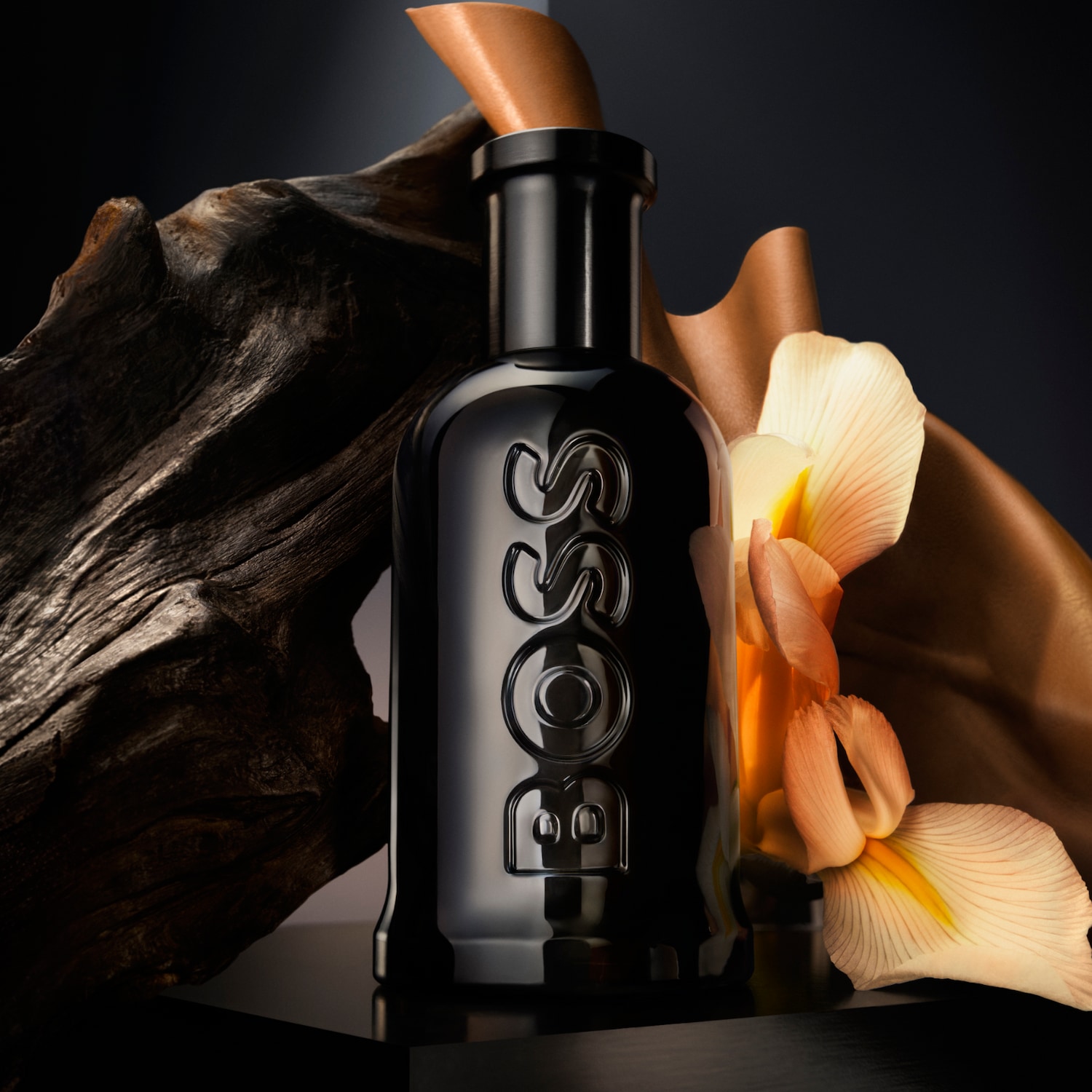 Czarny flakon perfum BOSS z drewnianym elementem i kwiatem, tworzący elegancką kompozycję.