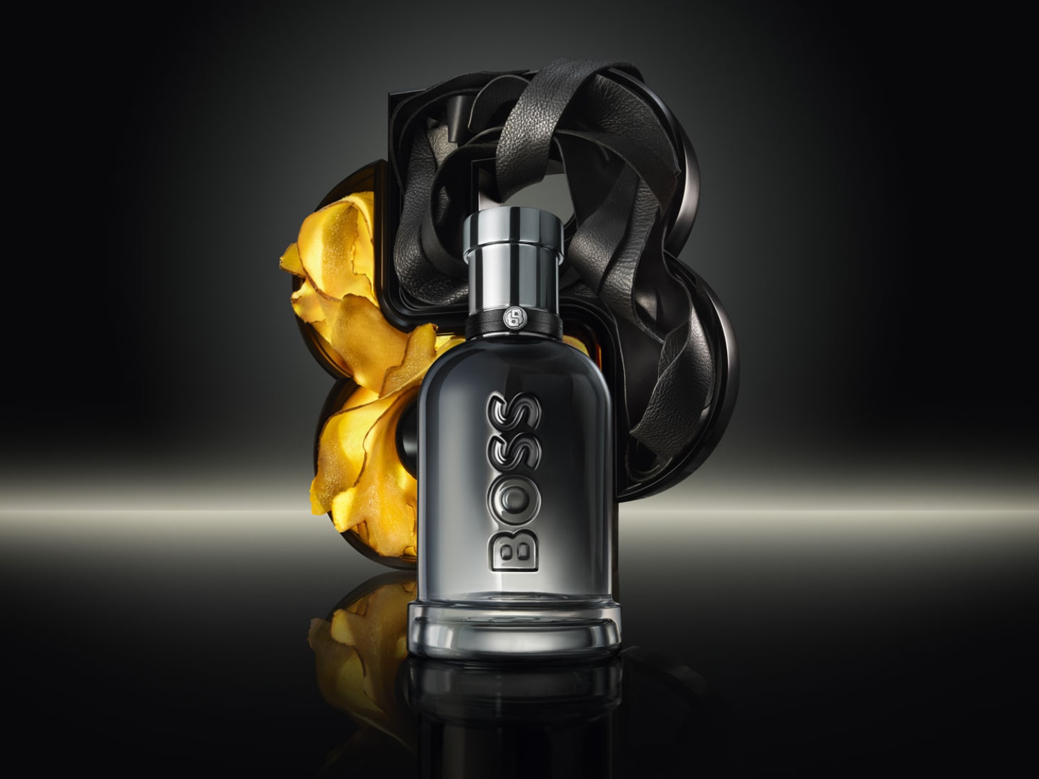 Elegancki flakon BOSS w odcieniach szarości i srebra, z nazwą marki pionowo wytłoczoną na butelce, otoczony złotymi i czarnymi akcentami, tworzy luksusową kompozycję.