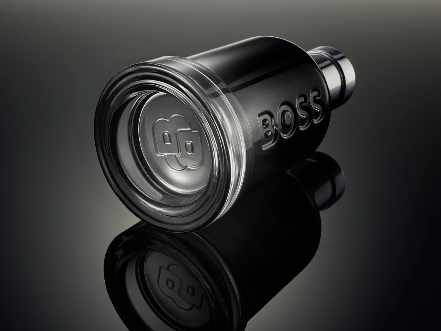 Czarny flakon perfum BOSS leży na boku, ukazując przezroczyste dno z logo marki i srebrną szyjkę.