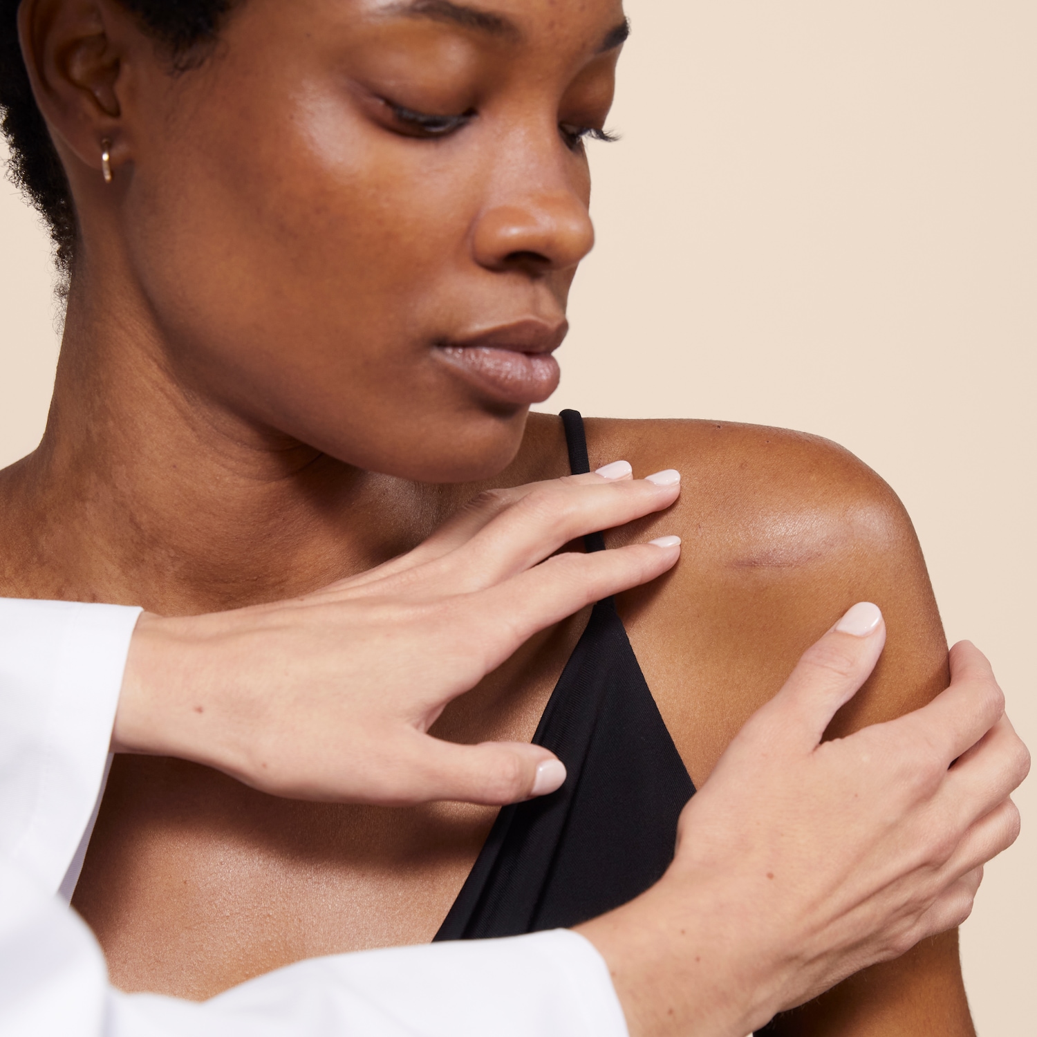 Une femme à la peau foncée se fait examiner l'épaule par un médecin portant une blouse blanche.
