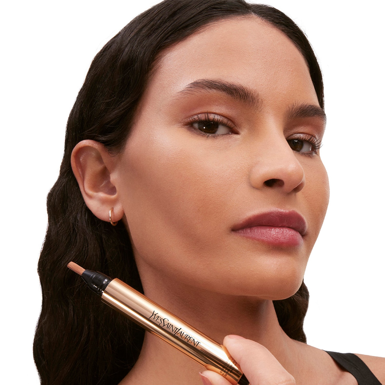 Une femme tient un stylo correcteur doré YVES SAINT LAURENT, le teint est uniforme et lumineux.